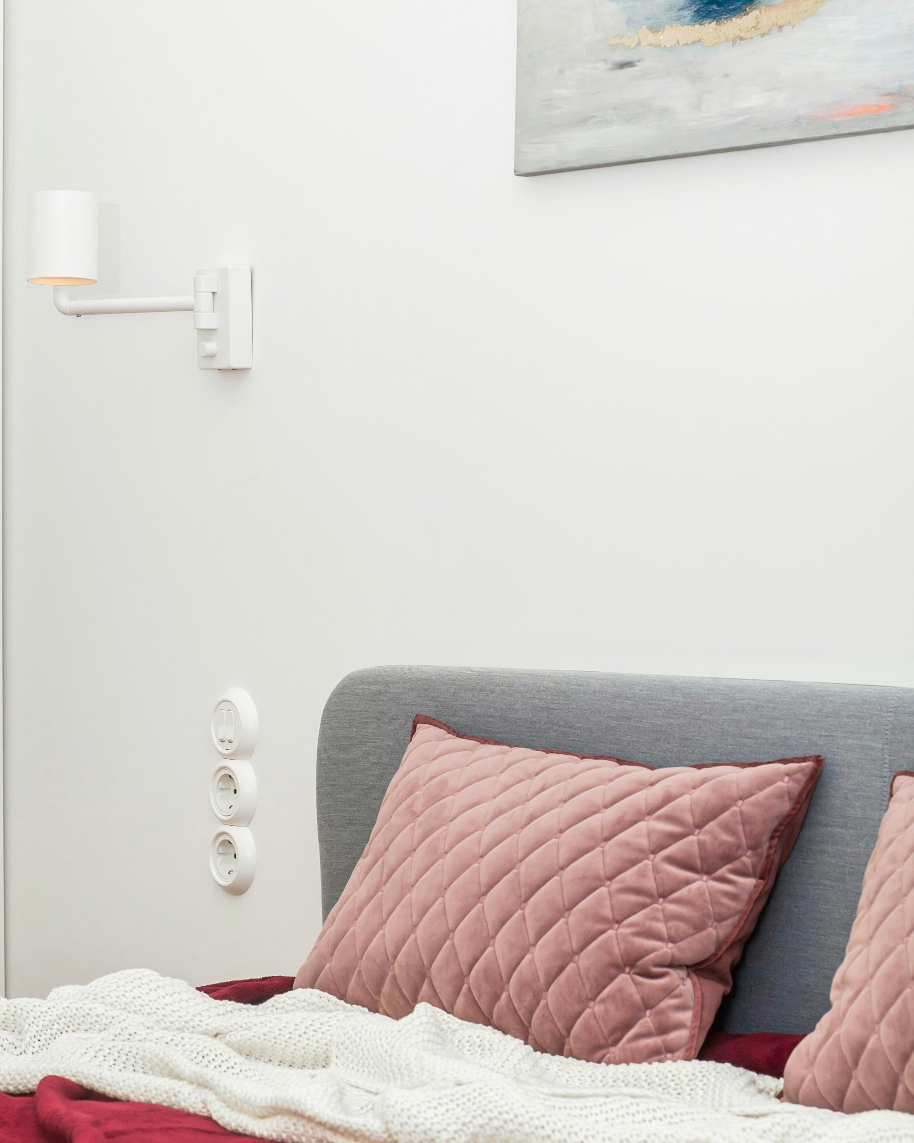 Bed with pink cushions and a deep red throw