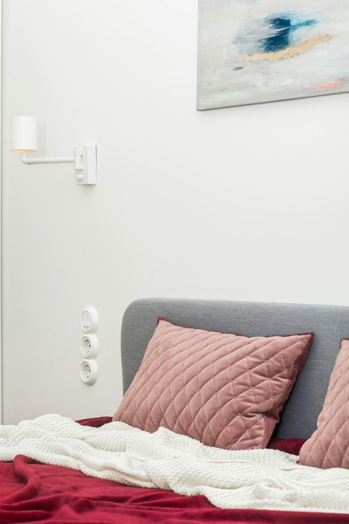 Bed with pink cushions and a deep red throw